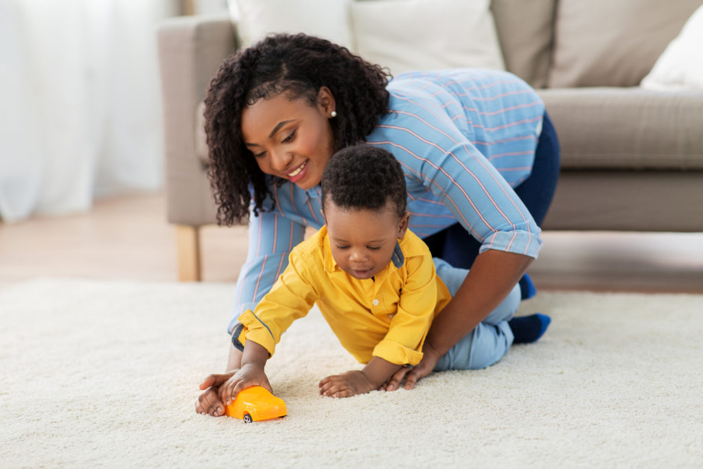 african american child playing with toy on the floor with the assistance of therapist